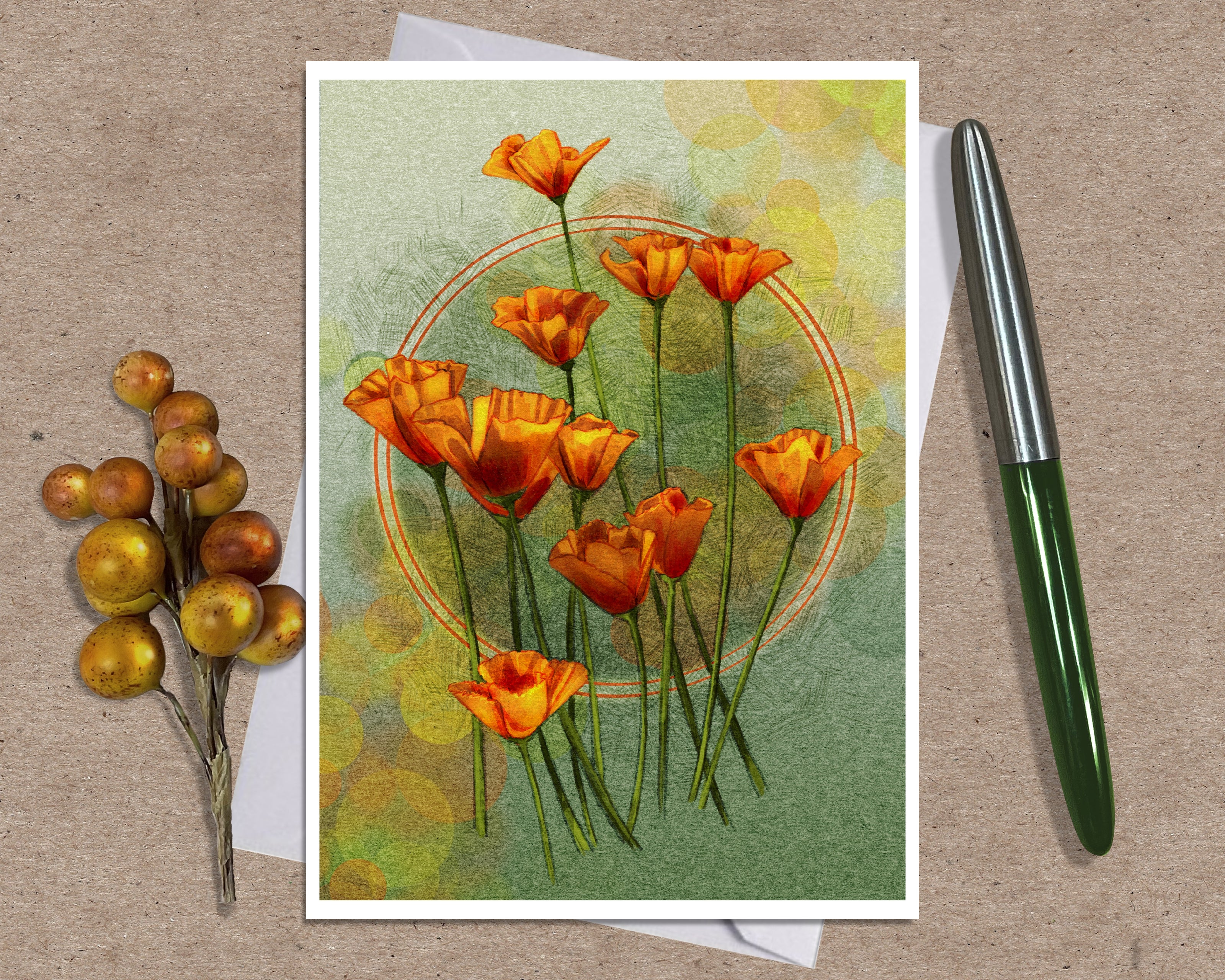 An art print greeting card featuring orange poppy flowers on a textured green and yellow background, styled on a kraft paper surface with a white envelope, a green and silver pen, and a small decorative berry sprig.