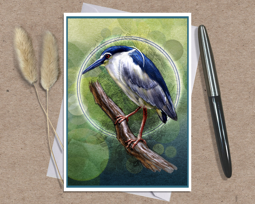 A square art print featuring a detailed illustration of a blue and white heron perched on a branch against a green bokeh background, styled on a brown textured surface with a black pen and dried grass stems.