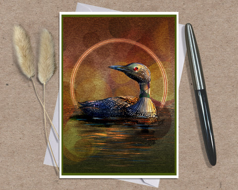 A square art print featuring a loon duck in water with a glowing circular light behind it, styled on a kraft paper background with two dried grass stems on the left and a black pen on the right.
