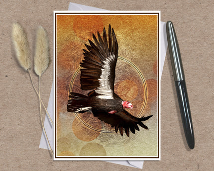 A square art print featuring a detailed illustration of a dark bird with spread wings over a textured orange and beige background, styled on a kraft paper surface with a pen and dried grass stems.
