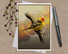 A square art print featuring a yellow and orange bird perched on a branch, styled on a kraft paper background with a white envelope, a silver pen, and decorative berries.