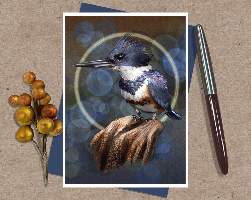 An illustrated greeting card featuring a Belted Kingfisher bird on a blue background with abstract glowing bubble orbs behind it. Posed with a sprig of yellow berries, an ink pen, and a dark blue envelope.