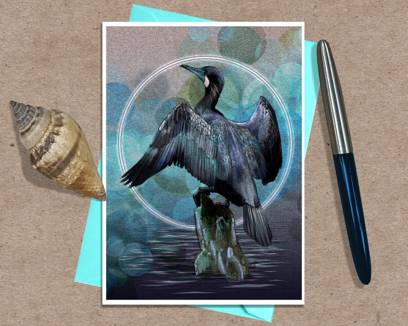 An art print greeting card featuring a dark bird perched on a rock against a blue-green bokeh background with a white circular frame, styled on a kraft paper surface with a turquoise card, a seashell, and a blue pen.