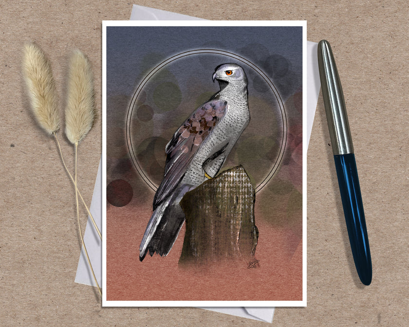 An art print greeting card featuring a detailed illustration of a bird of prey perched on a tree stump, set against a textured background with abstract circular patterns. The print is styled on a brown kraft paper surface with a white envelope underneath, flanked by two dried bunny tails on the left and a silver and blue pen on the right.