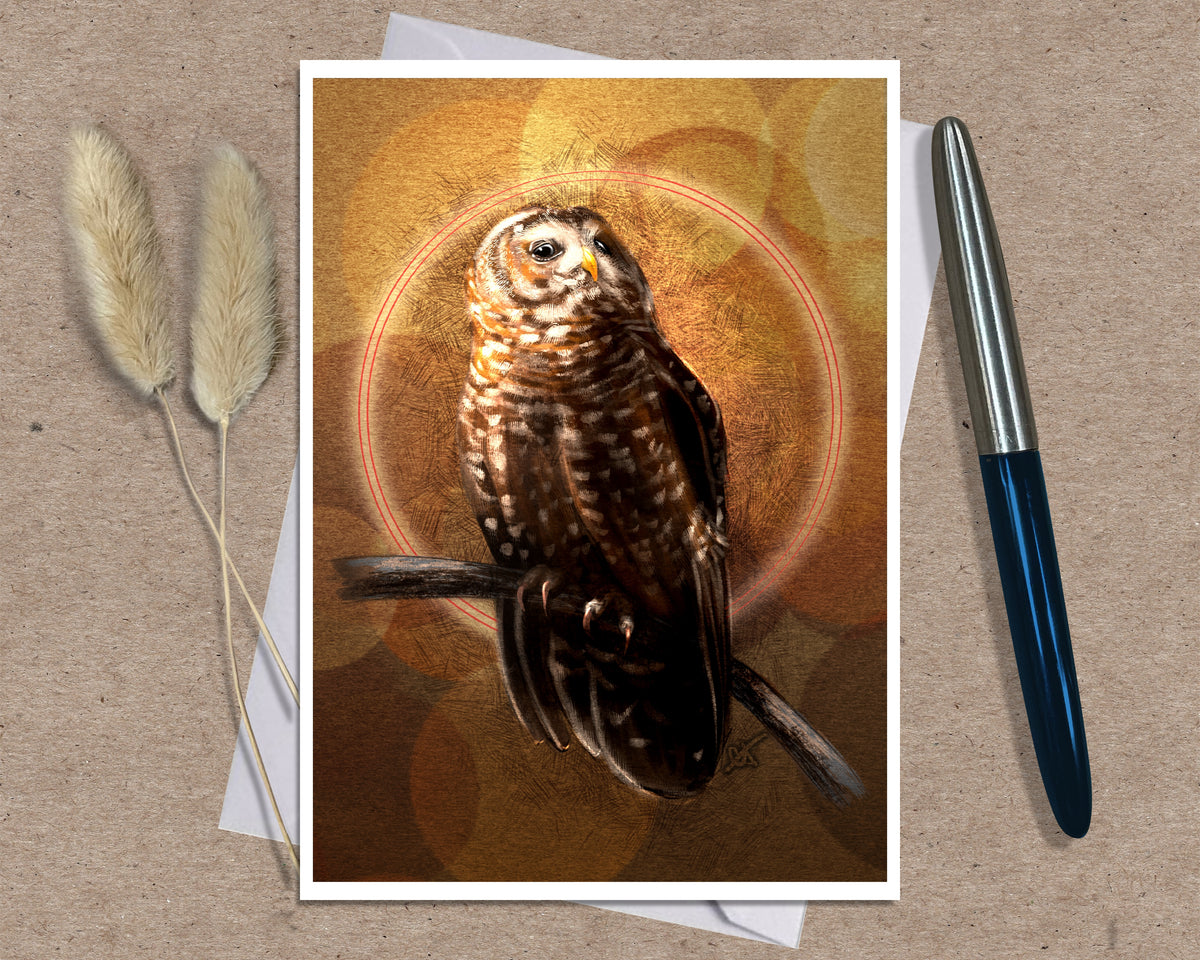 A greeting card featuring a detailed illustration of a brown owl perched on a branch against a warm golden-brown bokeh background. The print is displayed on a textured beige surface with a white pen on the right and two dried bunny tails on the left.