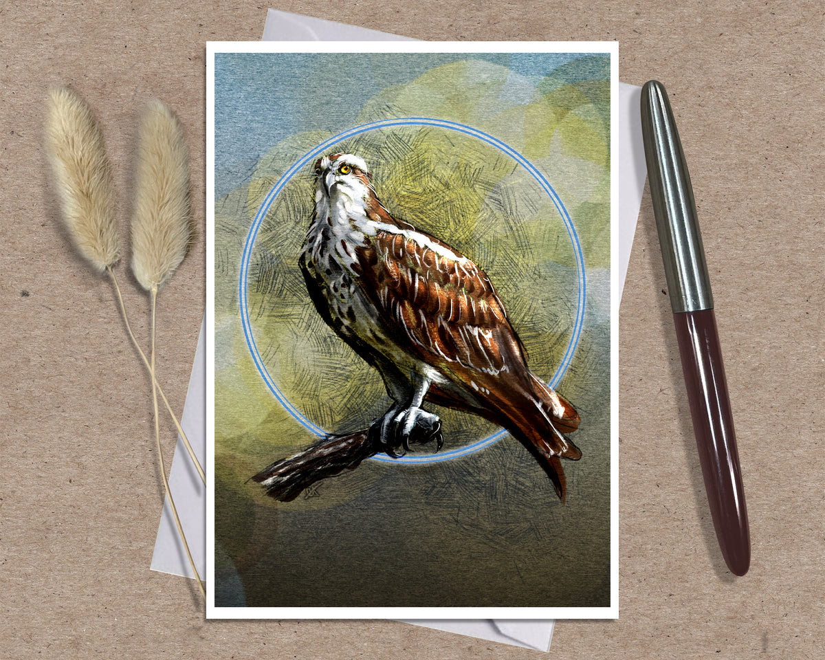 A greeting card featuring a detailed illustration of an osprey perched against a circular blue ring on a textured green and brown background, styled on a kraft paper surface with two dried reeds and a silver pen.