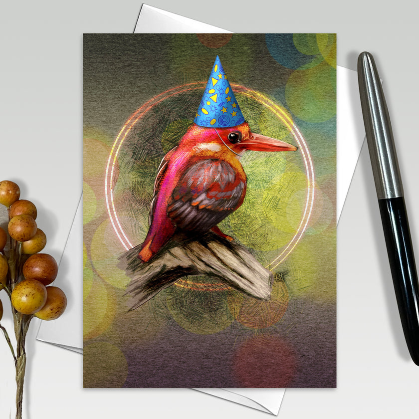 Greeting card with a colorful bird wearing a party hat on a white surface with a pen and decorative elements.