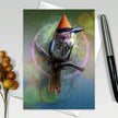 Greeting card with a bird wearing a party hat on a branch, surrounded by decorative elements.