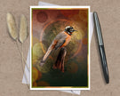 An art print greeting card featuring a detailed illustration of a bird perched on a branch, set against a textured abstract background with bokeh circles. The print is styled on a kraft paper background with a silver pen on the right and dried pampas grass on the left.