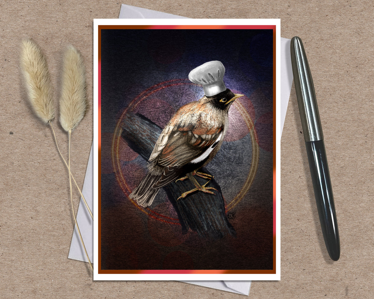 A greeting card featuring a bird perched on a log with a white chef's hat, styled on a kraft paper background with a silver pen and dried grass stems.