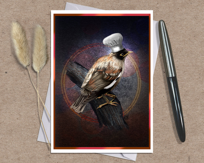 A greeting card featuring a bird perched on a log with a white chef's hat, styled on a kraft paper background with a silver pen and dried grass stems.