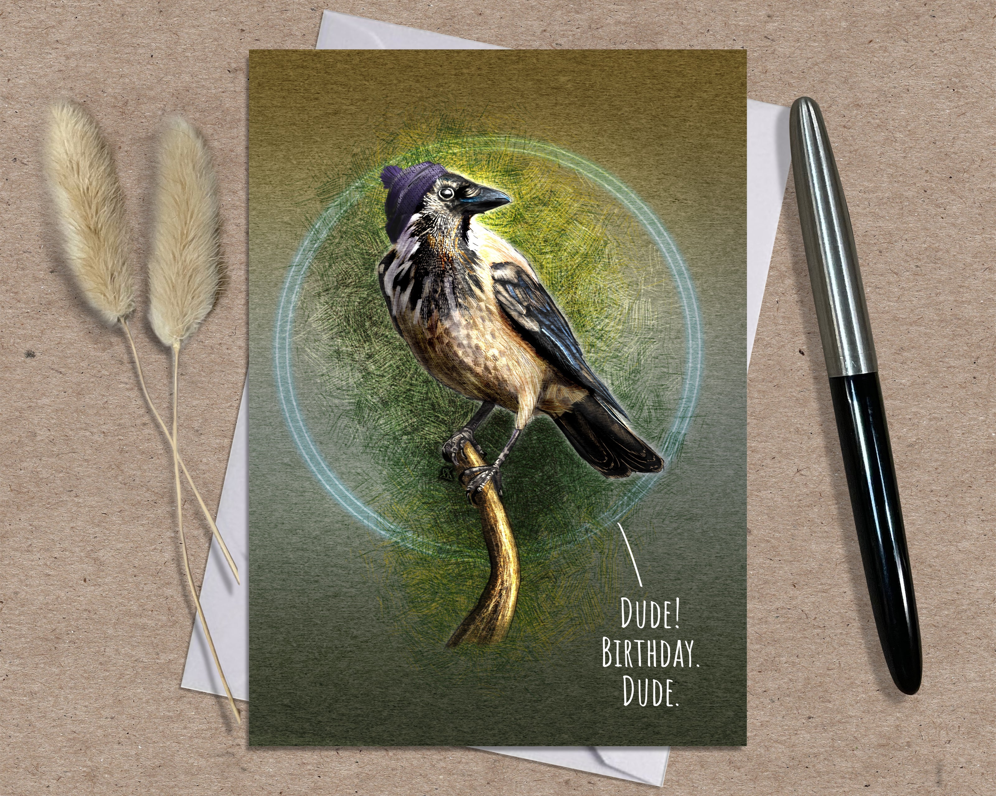 Greeting card with a bird illustration and text 'Dude! Birthday, Dude.' on a brown surface with a pen and dried plants.