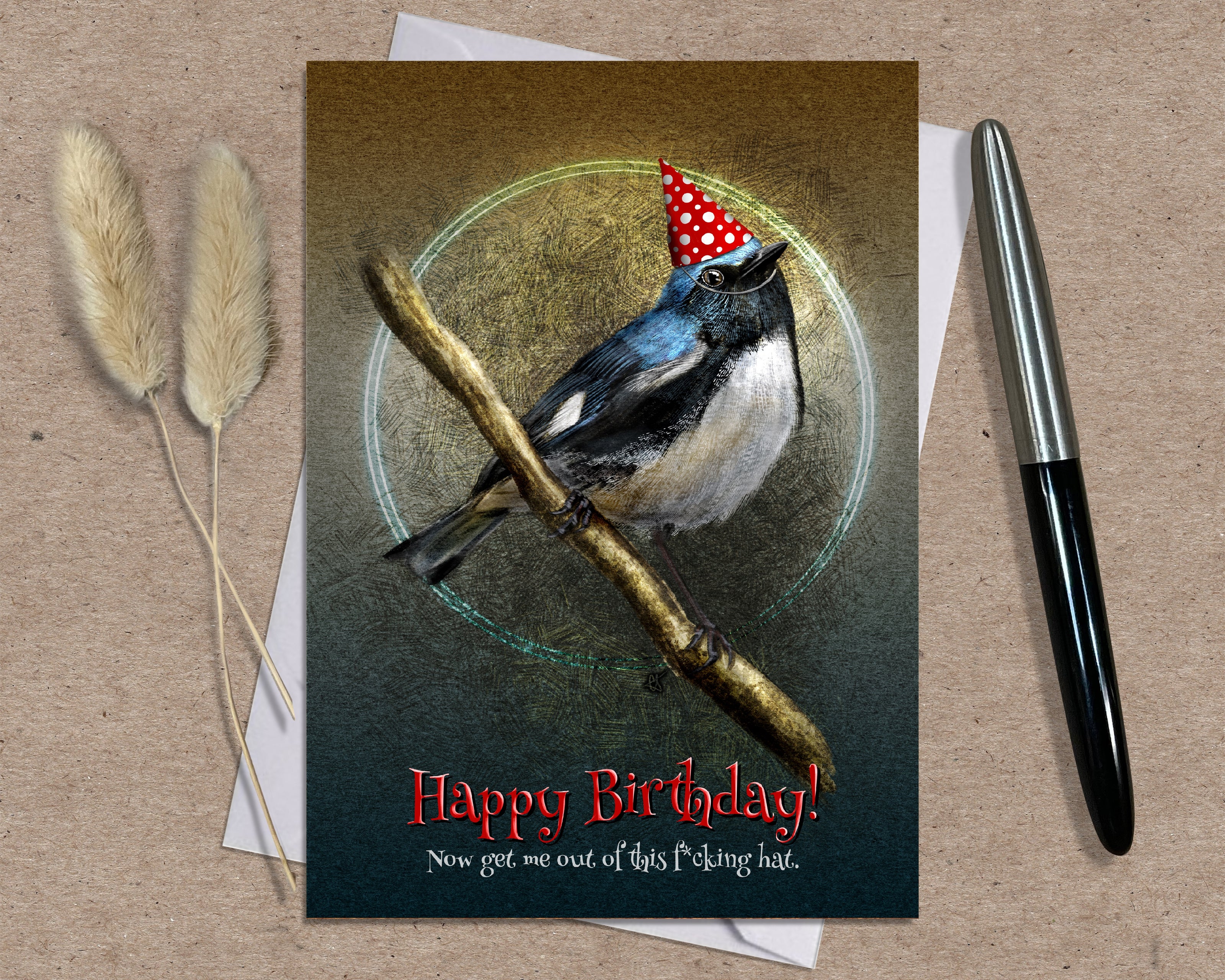 Birthday card with a bird wearing a party hat on a branch, placed on a textured surface with a pen and dried plants.