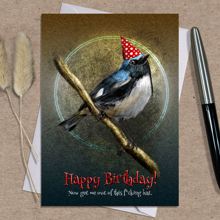 Birthday card with a bird wearing a party hat on a branch, placed on a textured surface with a pen and dried plants.
