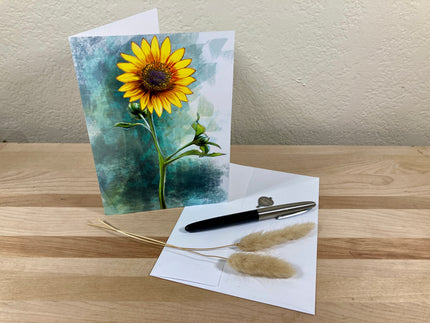 Greeting card with sunflower design on a wooden surface with a pen and dried plants.