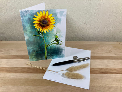 Greeting card with sunflower design on a wooden surface with a pen and dried plants.