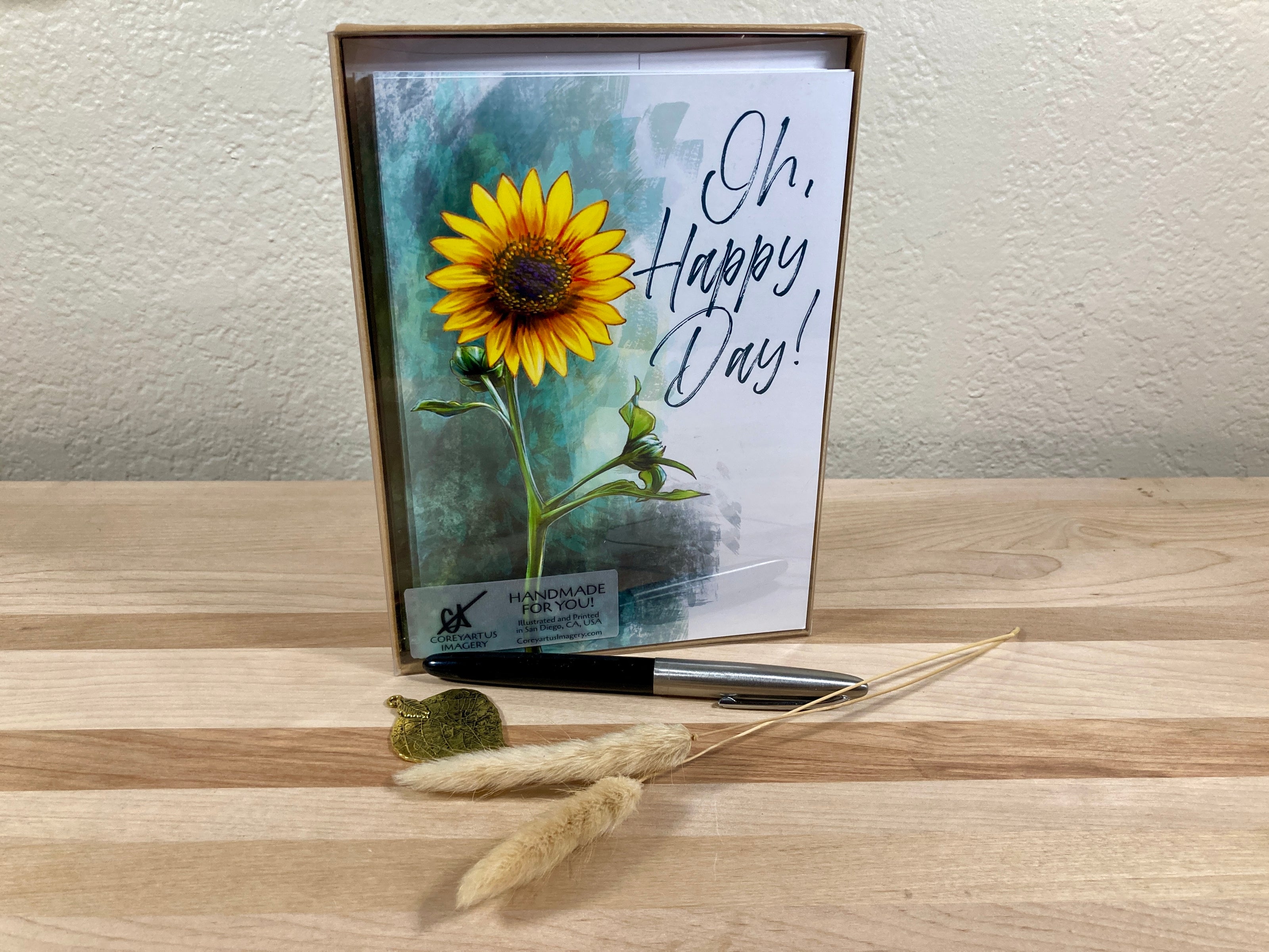 Card with sunflower design and 'Oh, Happy Day!' text on a wooden surface in a box package