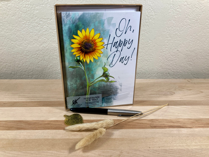 Card with sunflower design and 'Oh, Happy Day!' text on a wooden surface in a box package
