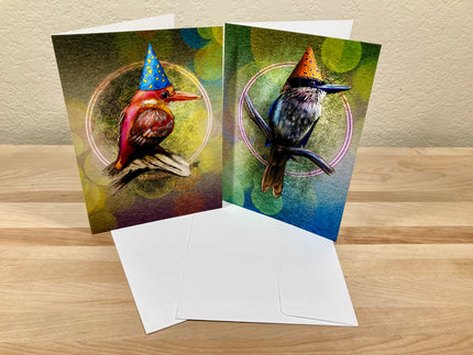 Two greeting cards with bird illustrations wearing party hats on a wooden surface.