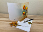 Greeting card with floral design on a wooden surface with a pen and decorative branch.