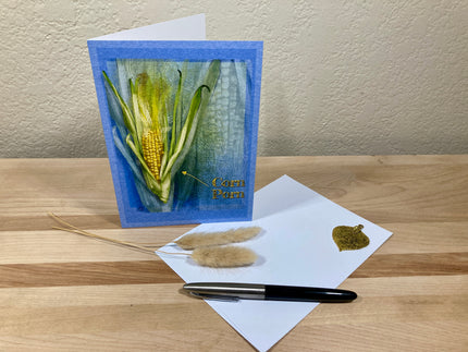 Greeting card with corn plant design on a wooden surface with a pen and paper.