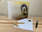 Greeting card with a bird illustration on a wooden surface with an envelope and pen.