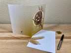 Greeting card with nature-themed design on a wooden surface with a pen and decorative elements.