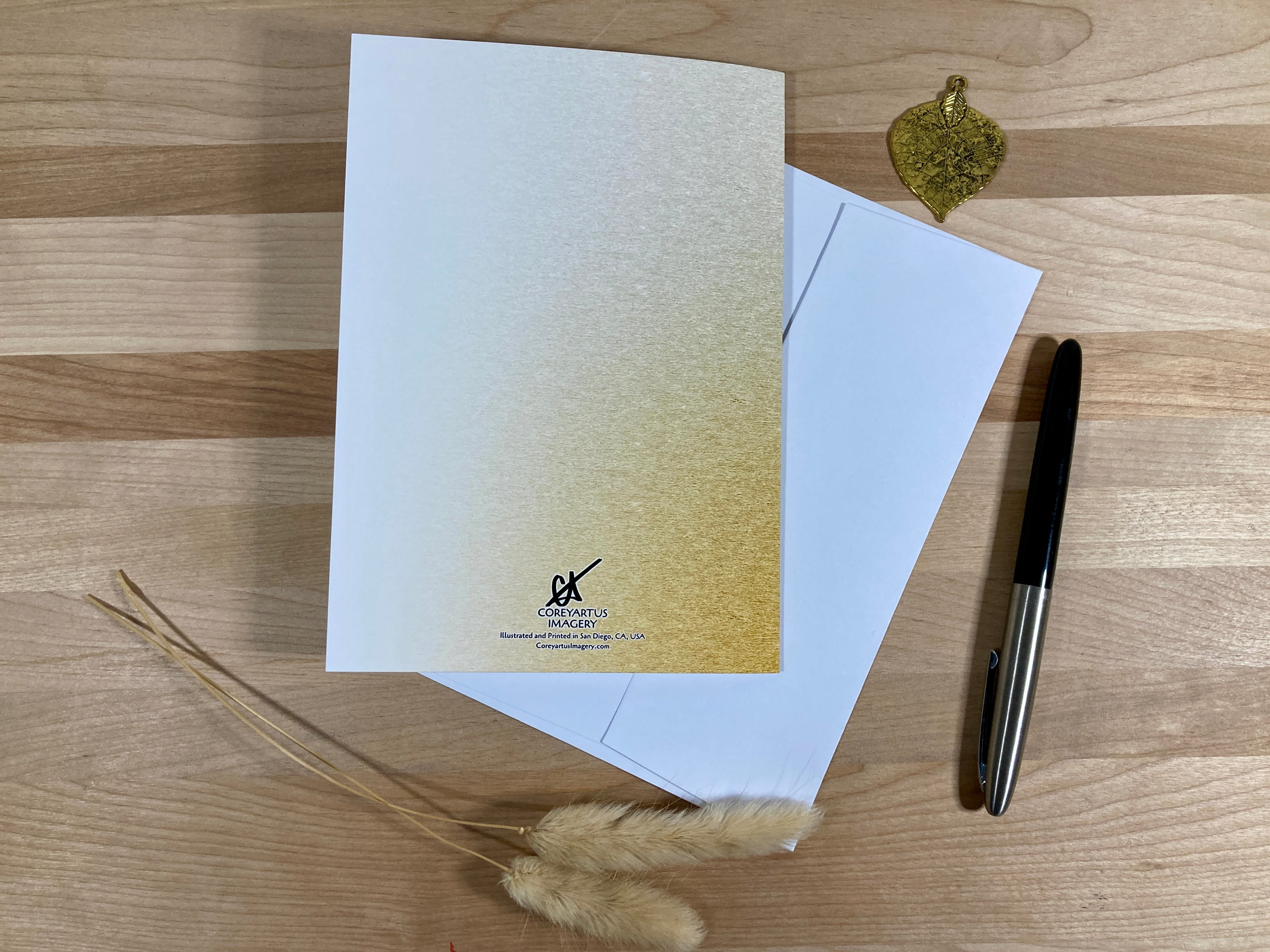 White card with gold gradient and logo on a wooden surface with a pen and decorative elements.