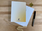 White card with gold gradient and logo on a wooden surface with a pen and decorative elements.