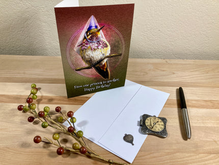 Greeting card with a hummingbird design on a wooden surface with a pen and decorative branch.