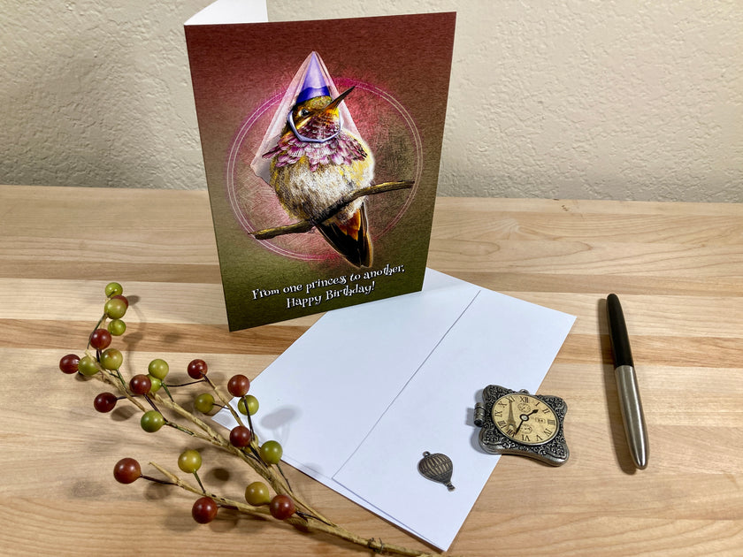 Greeting card with a hummingbird design on a wooden surface with a pen and decorative branch.