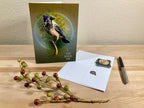 Greeting card with a bird design on a wooden surface with stationery items.