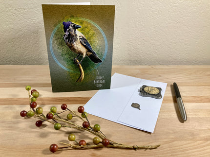 Greeting card with a bird design on a wooden surface with stationery items.