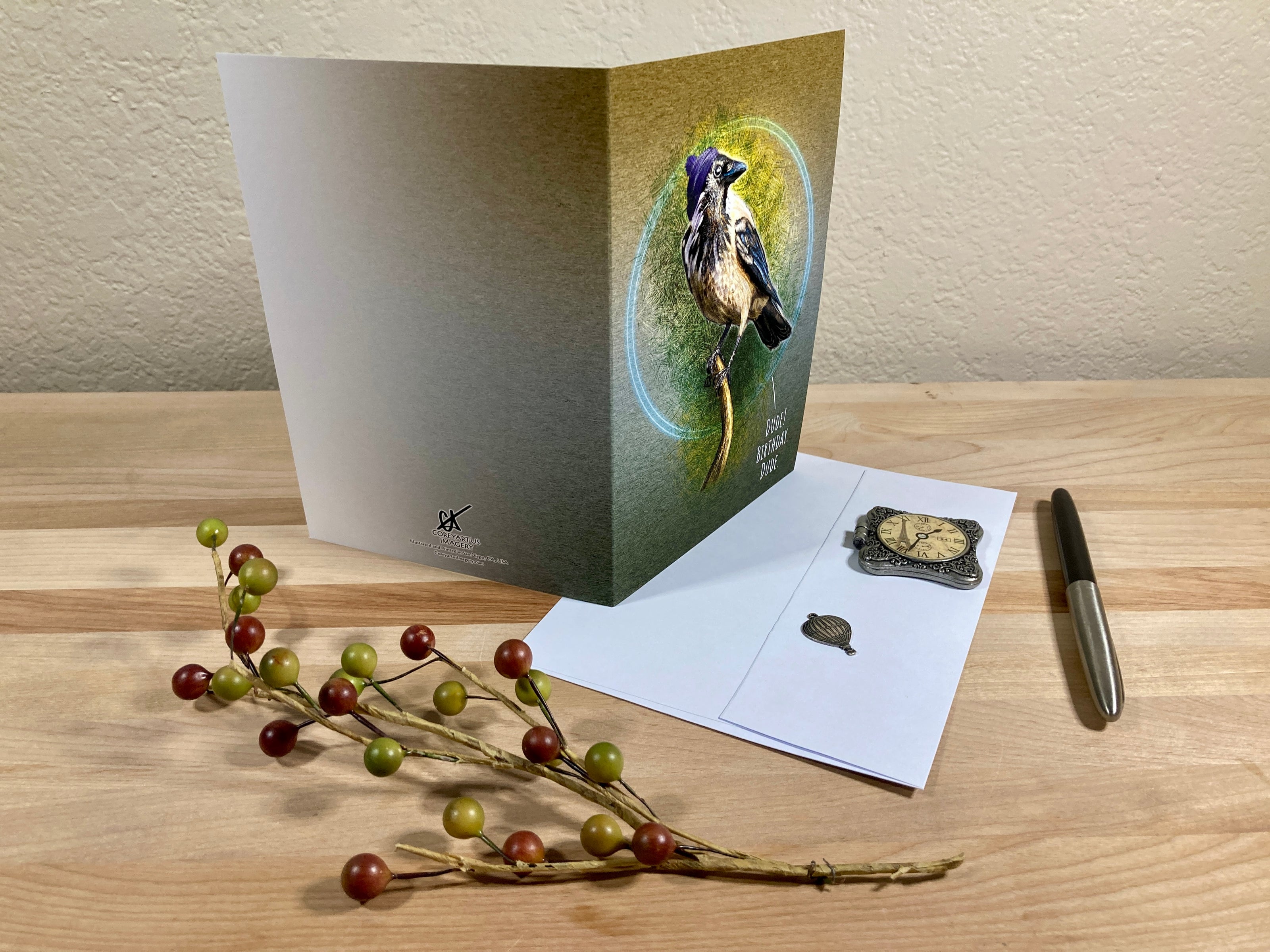 Greeting card with a bird design on a wooden surface with a pen and decorative branch.