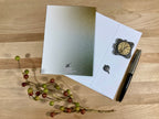 Greeting card with decorative pen and branch on a wooden surface