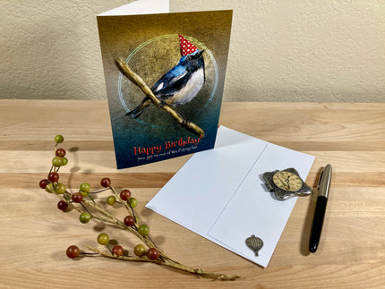 Birthday card with a bird design on a wooden surface with an envelope and decorative items.