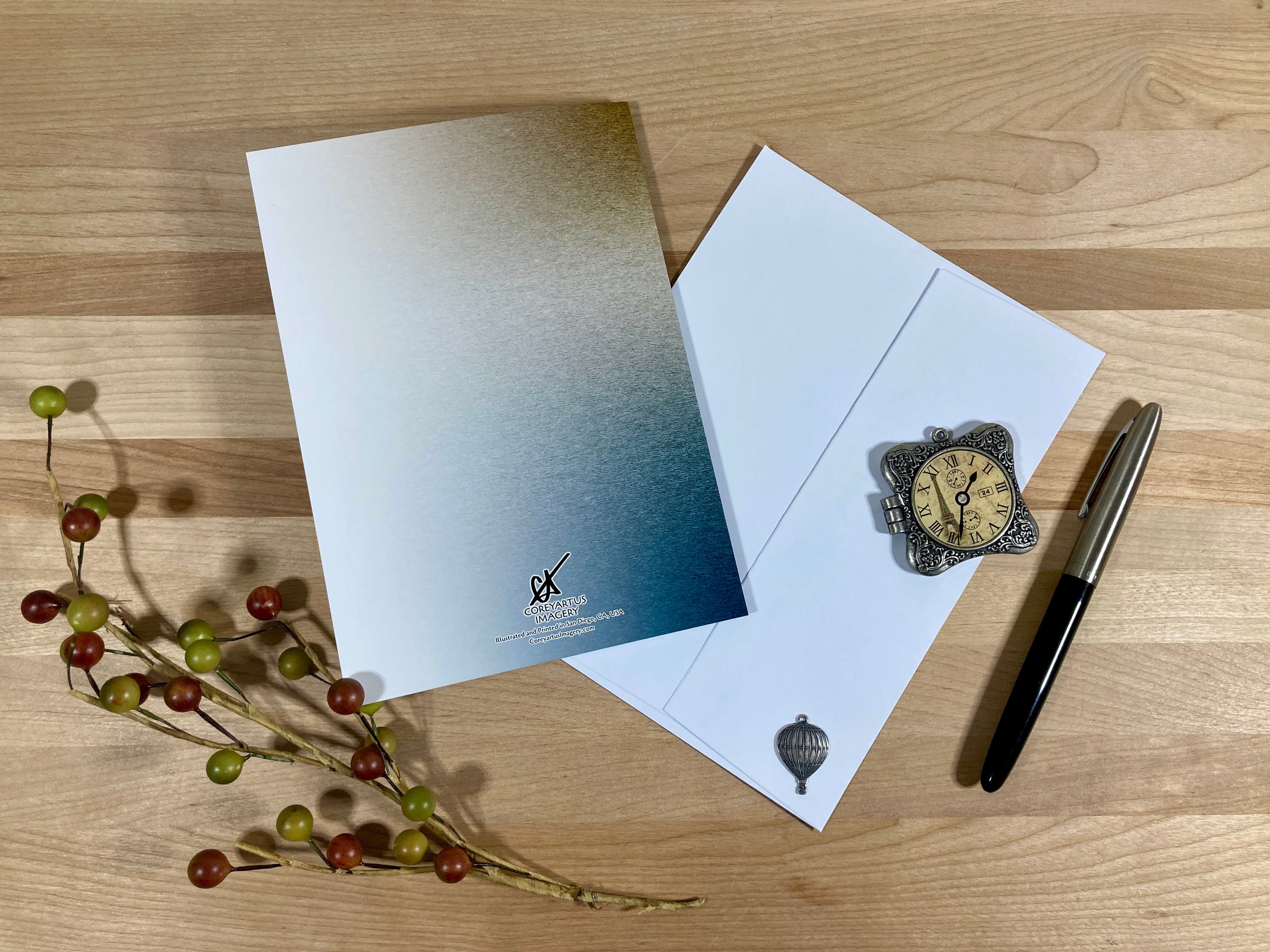 Greeting card, envelope, decorative watch, pen, and branches on a wooden surface
