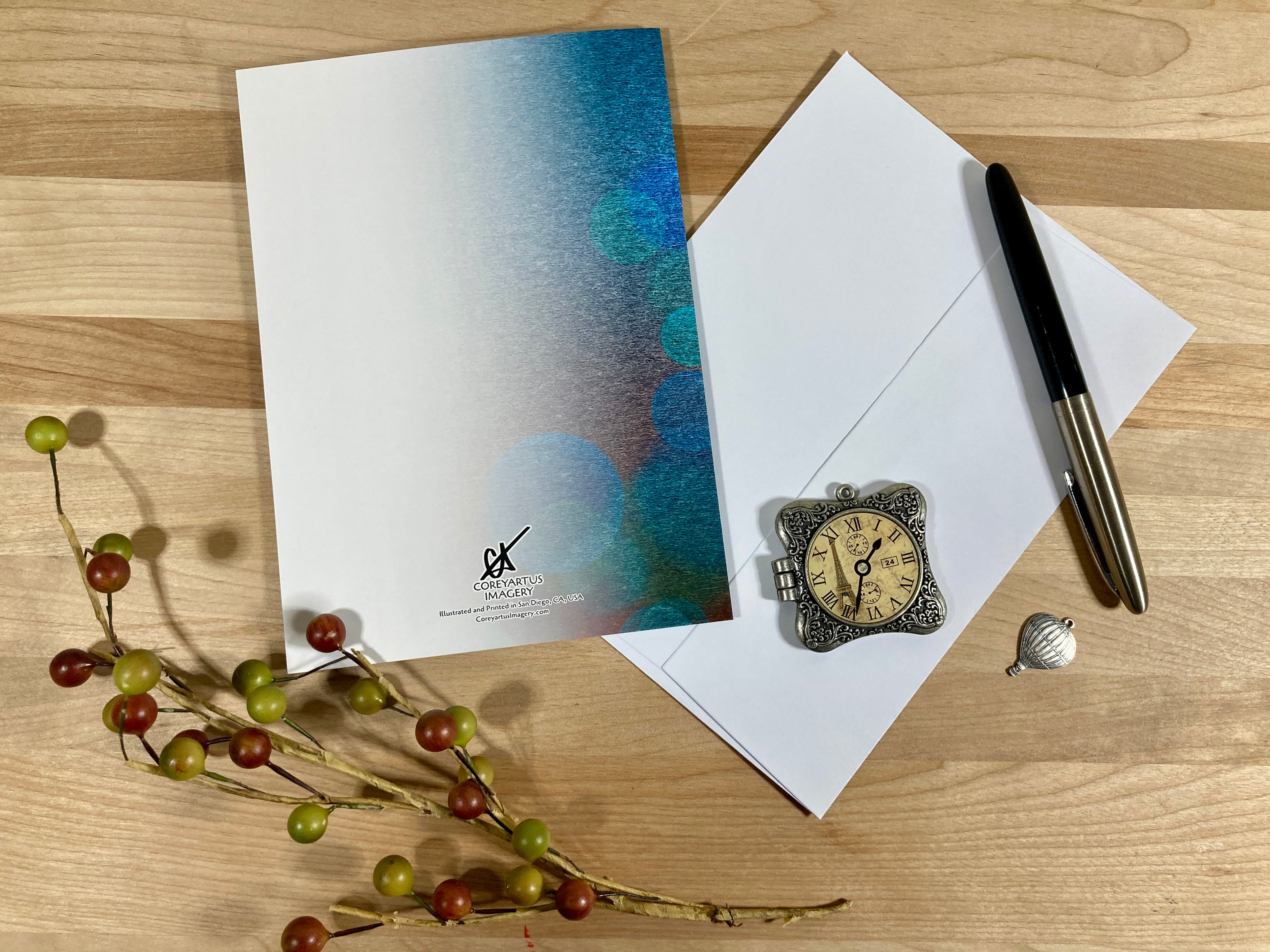 Greeting card, envelope, pen, decorative clock, and small shell on a wooden surface.
