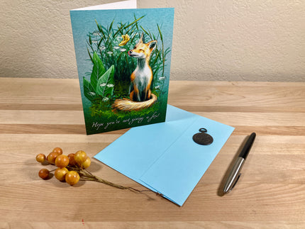 Greeting card with a fox illustration on a wooden surface with a pen and berries.