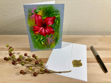 Floral greeting card with red flower, pen, and envelope on a wooden surface