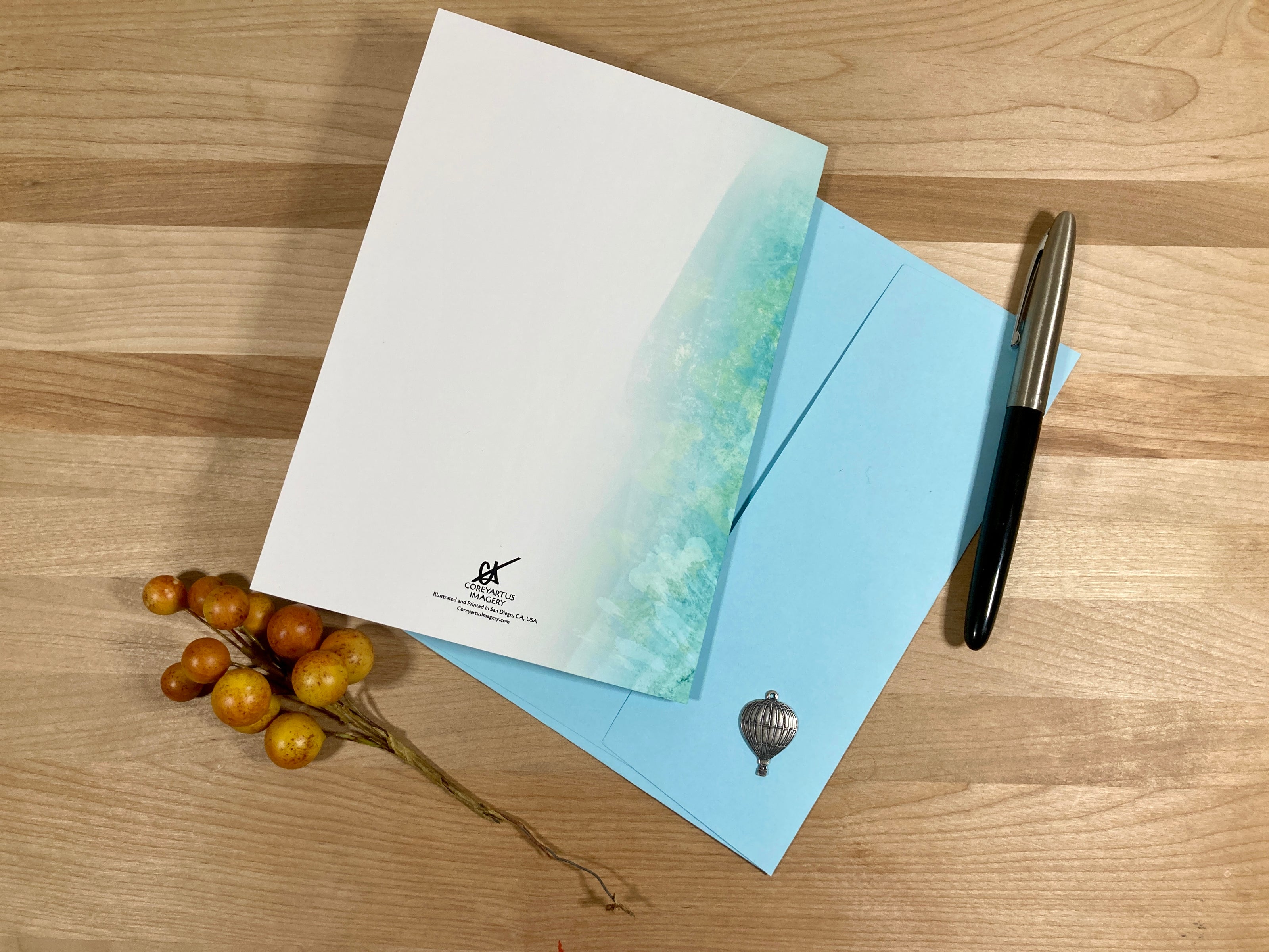 Letterhead, envelope, and pen on a wooden surface with decorative elements.