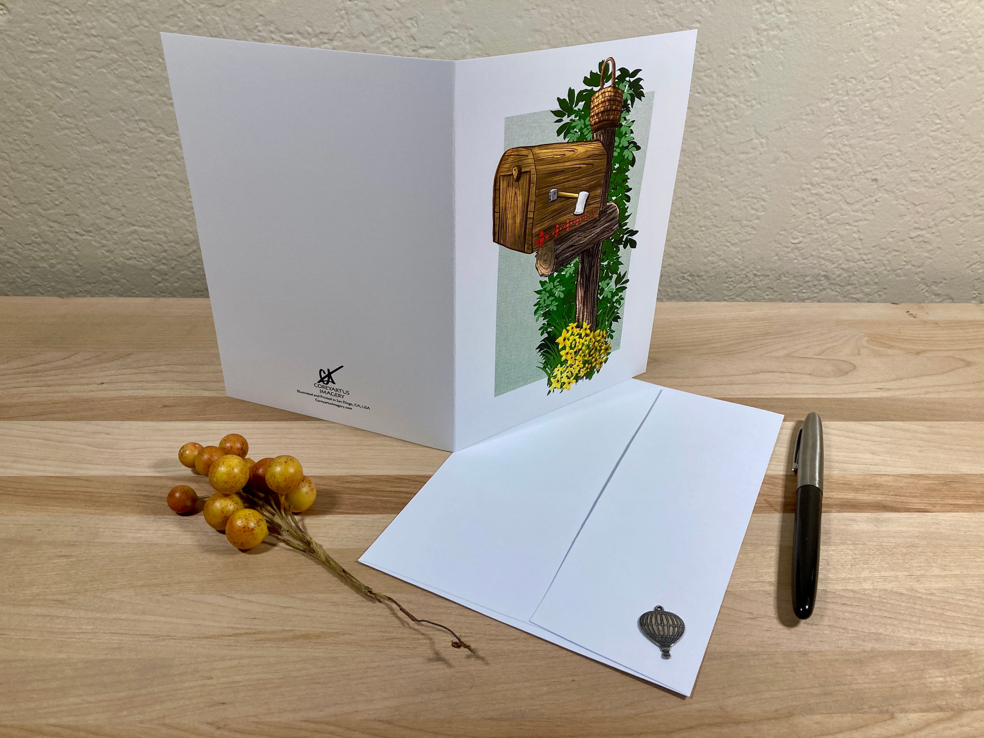 Greeting card with mailbox illustration on a wooden surface with envelope and decorative elements.
