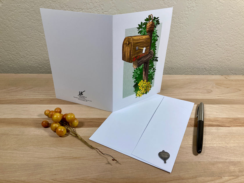 Greeting card with mailbox illustration on a wooden surface with envelope and decorative elements.