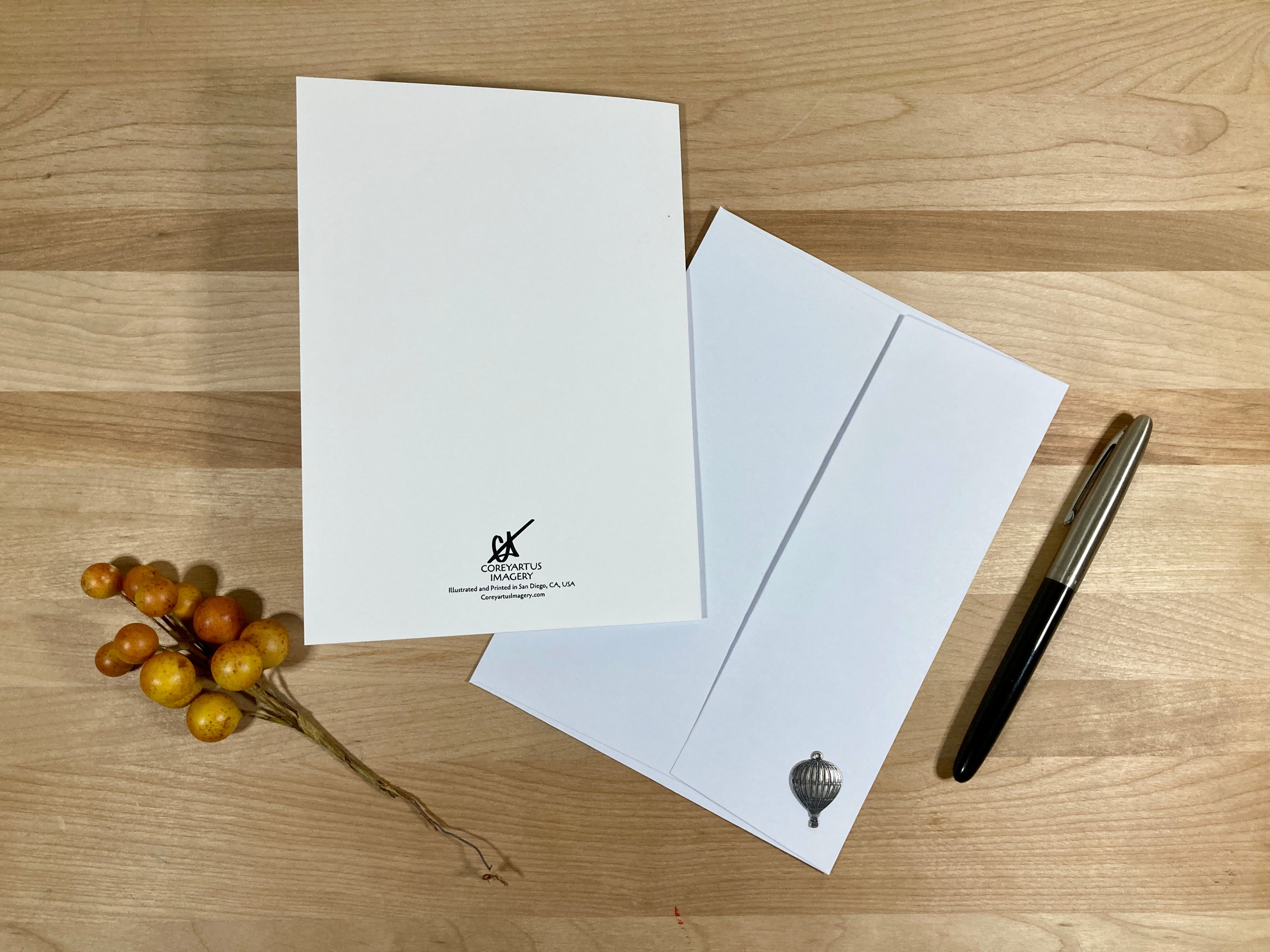 White letterhead paper with a logo, white envelope, pen, and decorative berries on a wooden surface