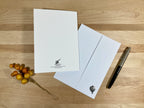 White letterhead paper with a logo, white envelope, pen, and decorative berries on a wooden surface