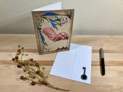 Decorative greeting card with artistic design on a wooden surface with a pen and branch.