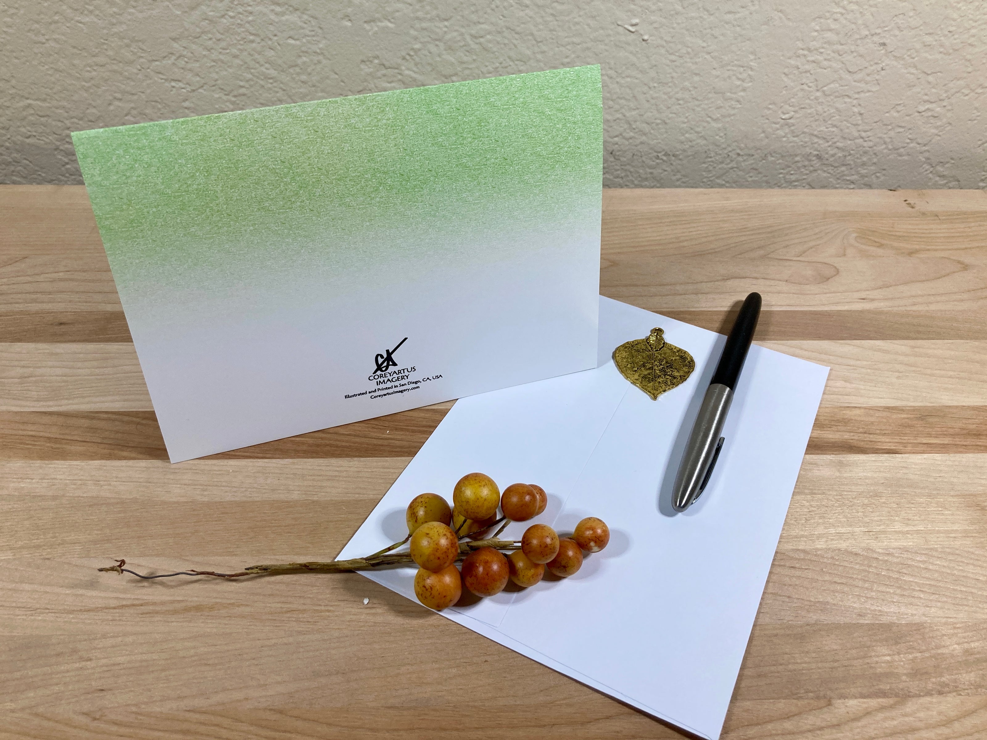 Greeting card with a pen and decorative branch on a wooden surface