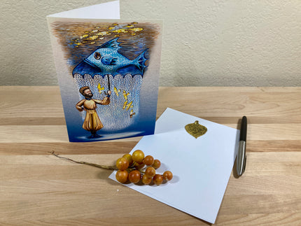 Greeting card with artistic design on a wooden surface with a white envelope and decorative stones.