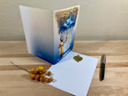 Greeting card with artistic design on a wooden surface with a pen and decorative item.