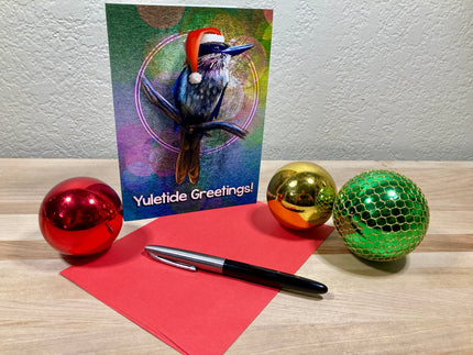 Christmas card with a bird wearing a Santa hat, surrounded by festive balls and a pen on a wooden surface.